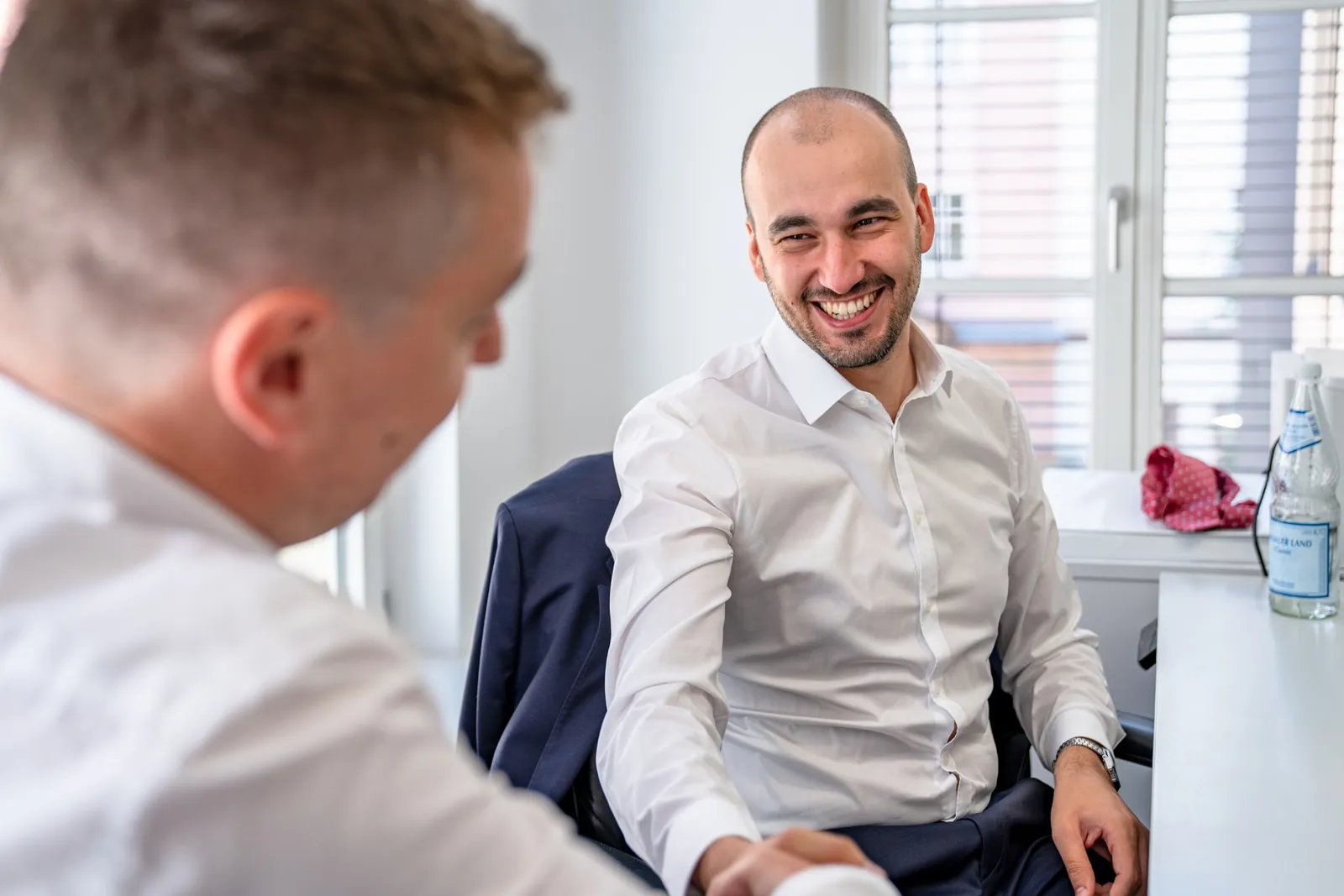 Zwei Kollegen lachen gemeinsam im Gespräch am Arbeitsplatz in Mainz