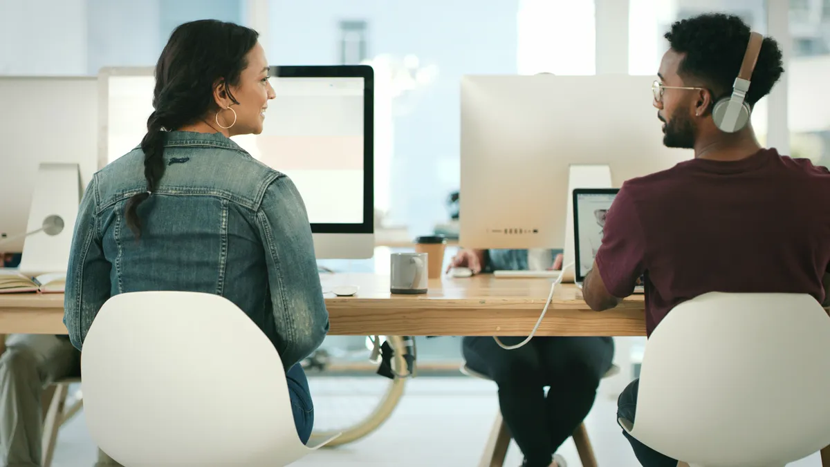 Zwei Mitarbeitende im Austausch an ihren Schreibtischen im modernen Büro – Employee Experience